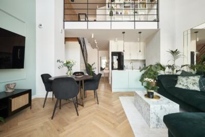 Modern living room with an open kitchen, a green sofa and a wooden floor.