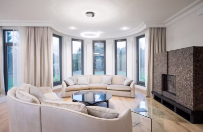 A modern living room with large windows, a beige sofa and a fireplace.