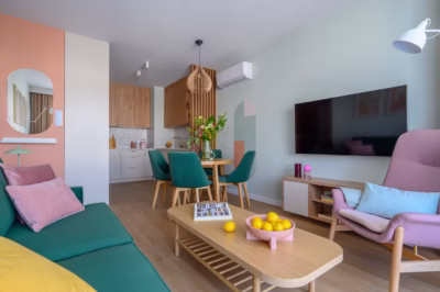 A modern living room with a green sofa, pink accessories and a wooden table.