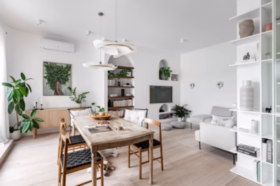 A bright interior with a wooden table, green plants, and bookshelves full of books.