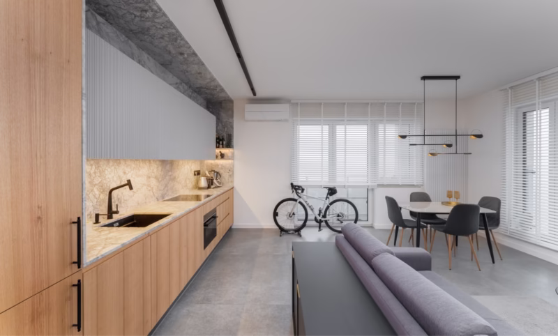 Modern kitchen with light marble, wooden cabinets and a bicycle in the background.