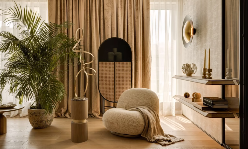 Beige and cream living room with large palm, round seat, wooden shelves.