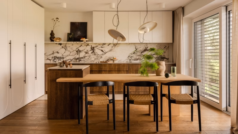 Kitchen with a wooden table and three black chairs, stone strip above the worktop.