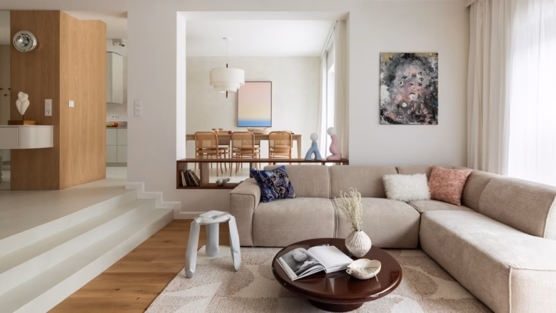 Living room with a beige corner sofa and a low round table by an open dining area.