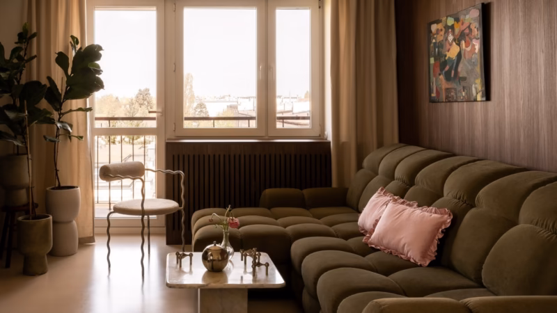 Quilted olive sofa with a pink cushion and a light coffee table by a large window.