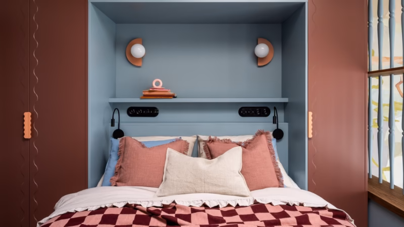 Bed in a blue recess with pink cushions and wall lights.
