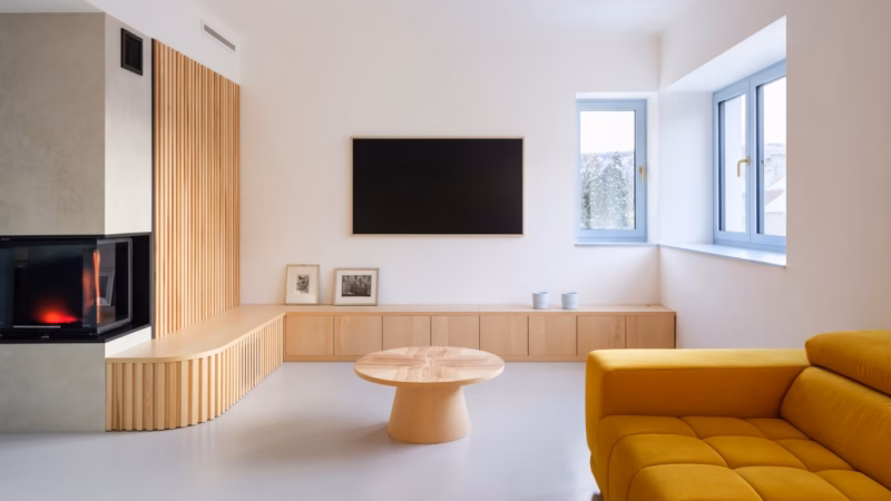 A living room with wooden fitted furniture, a black television and a mustard-coloured sofa