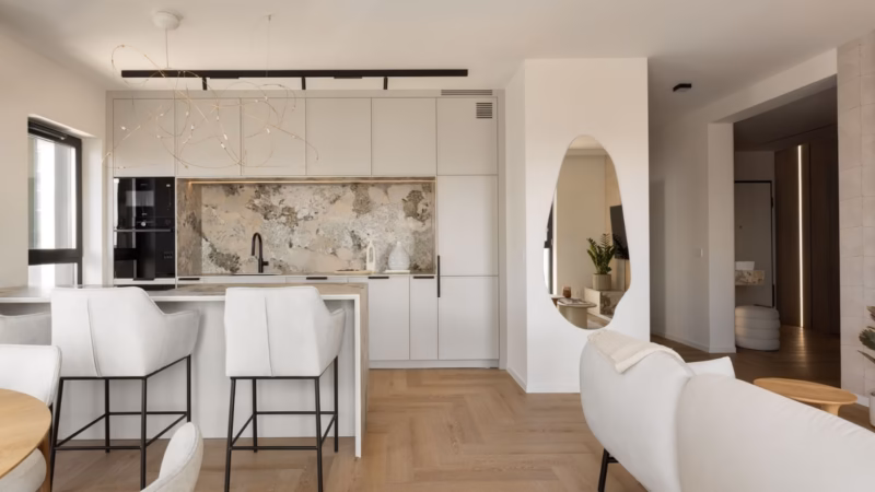 White kitchen with an island, a stone panel and black bar stools.
