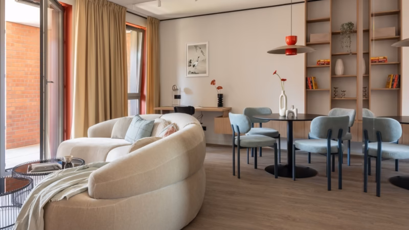 Living room with a rounded sofa, dining area and built-in shelving.