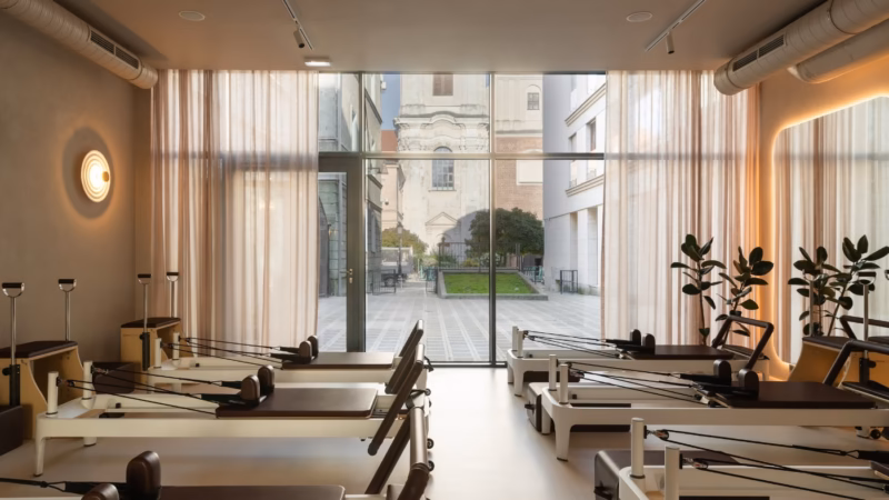 Pilates studio with rows of reformers and a view of a historic courtyard.