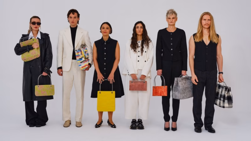 Six people in black, white and colourful outfits, carrying bags, against a light-coloured background